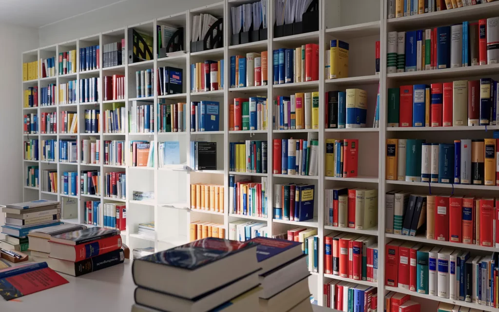 Große Wand mit geordneten Bücherregalen voller juristischer Fachbücher, Tisch mit aufgeschlagenen und gestapelten Büchern im Vordergrund