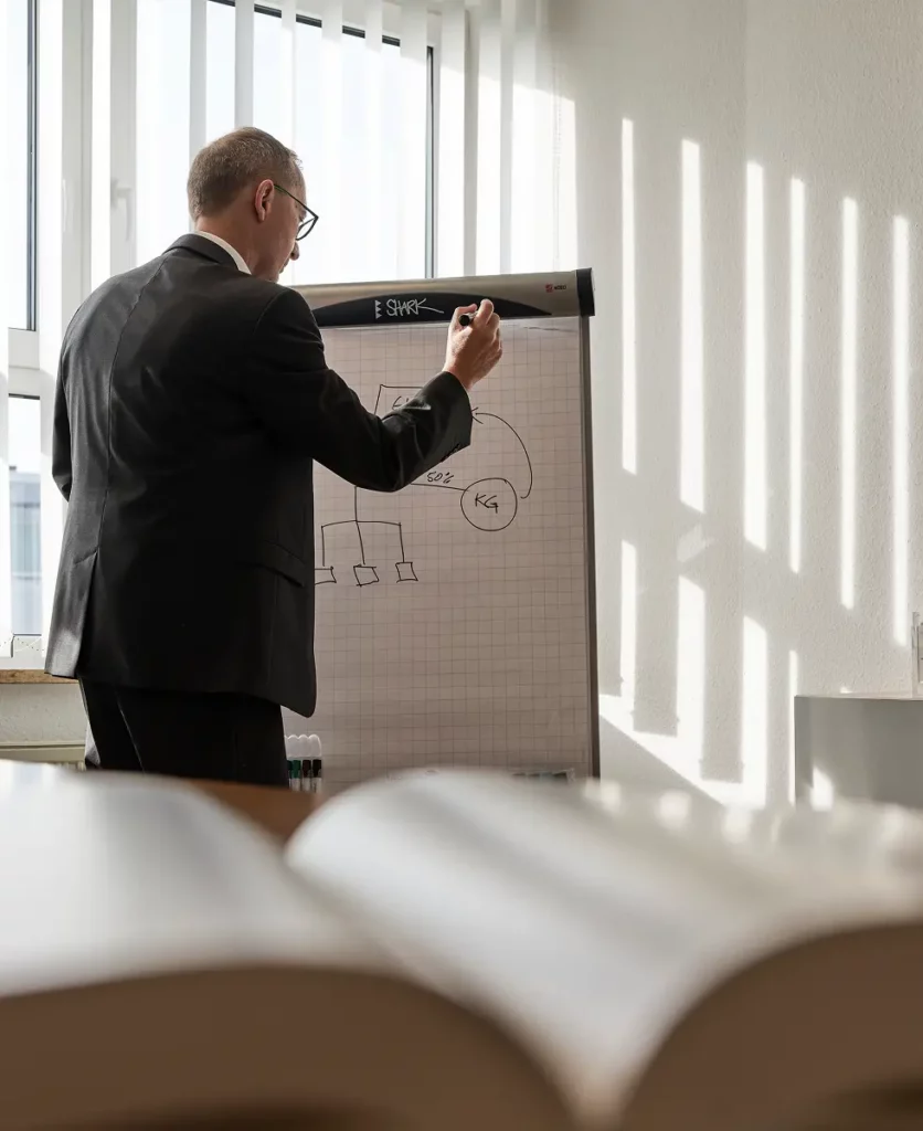 Person im Anzug steht an einem Flipchart und skizziert ein Diagramm